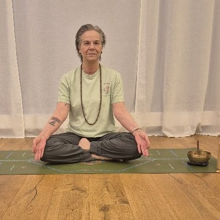 Shivanjali im Lotussitz auf der Yogamatte im Studio, daneben eine Klangschale